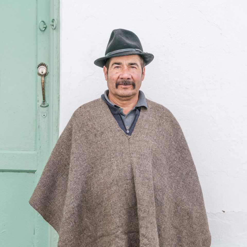 Older man wearing a poncho and dark hat