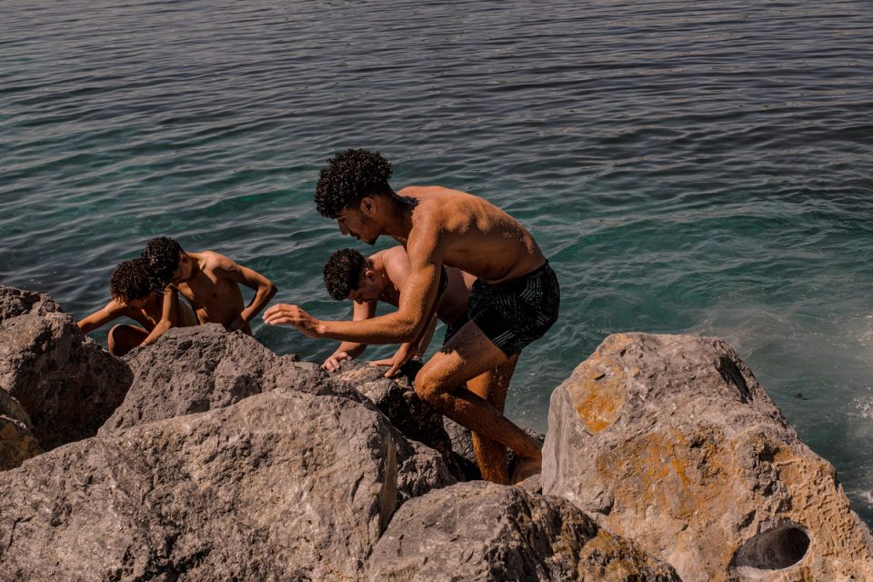 Three people resting on rocks by the sea