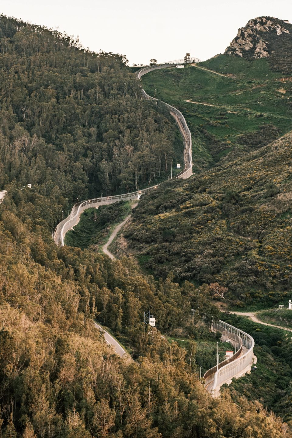 Winding border fence crossing green hills