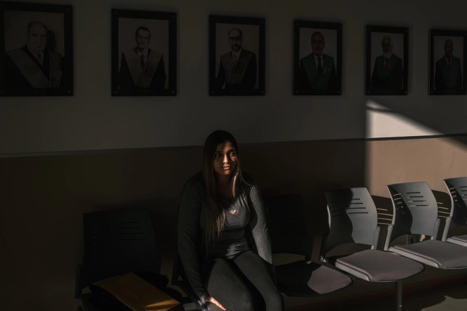 Woman sitting in a dim room beneath framed portraits