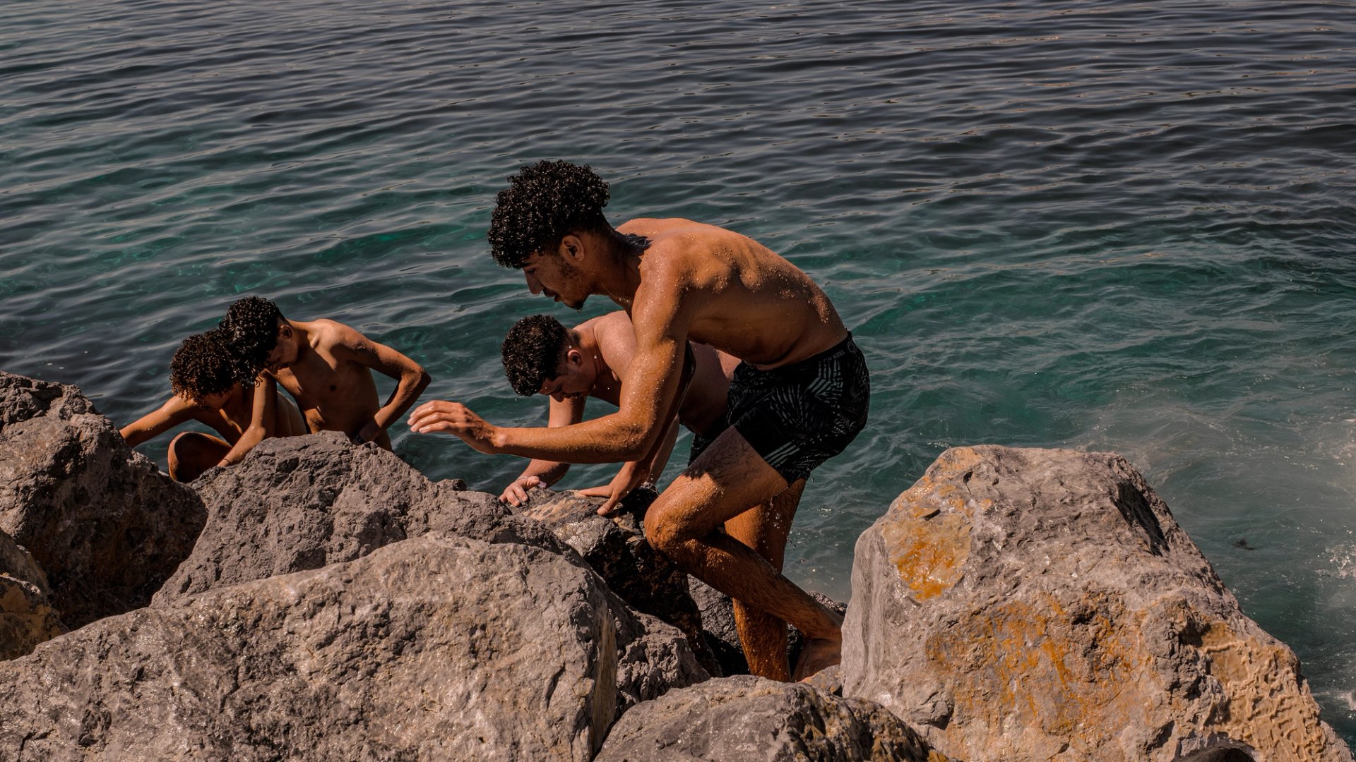 Three people resting on rocks by the sea