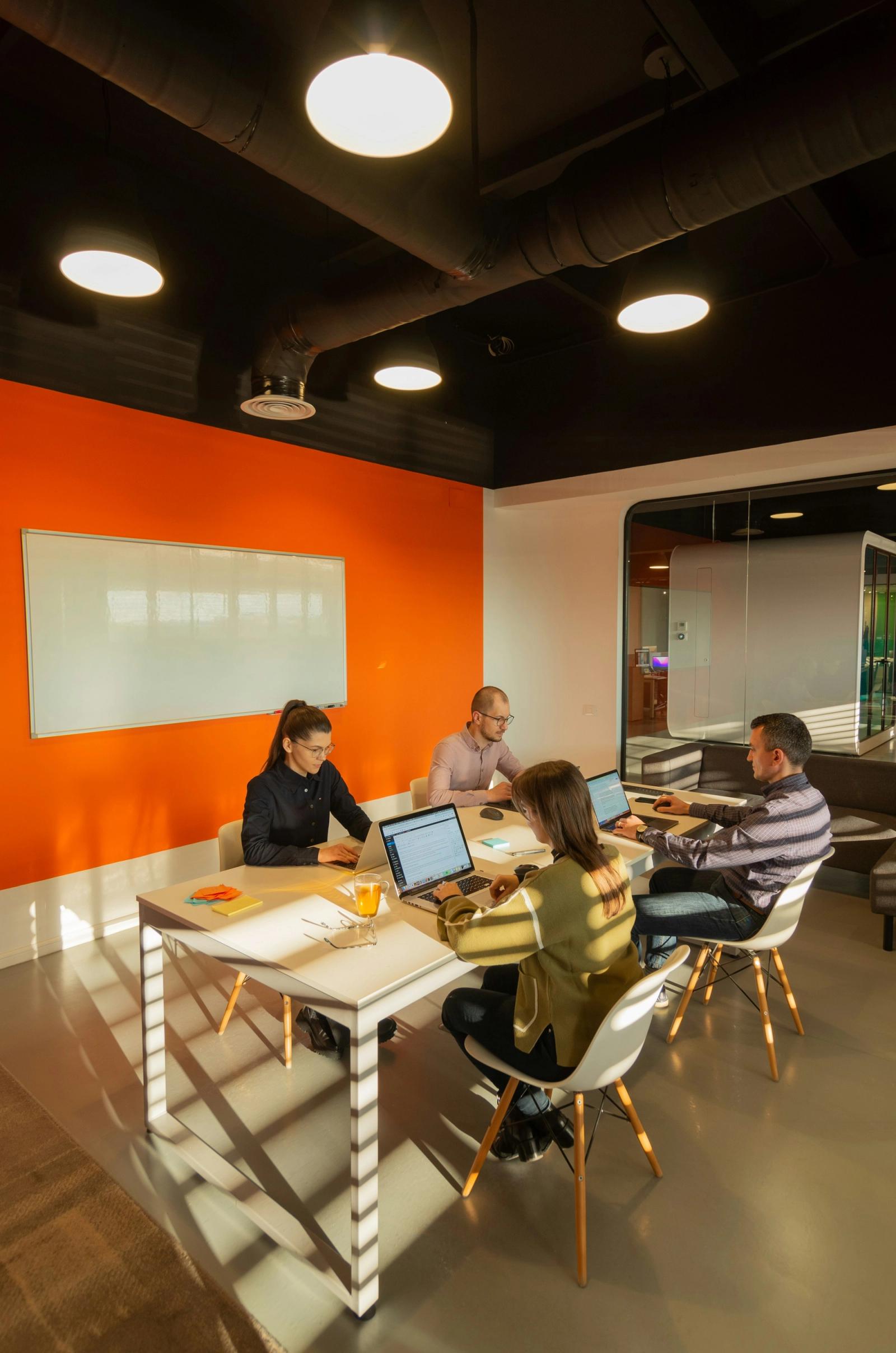 A team of four working on laptops around a table in a modern meeting room