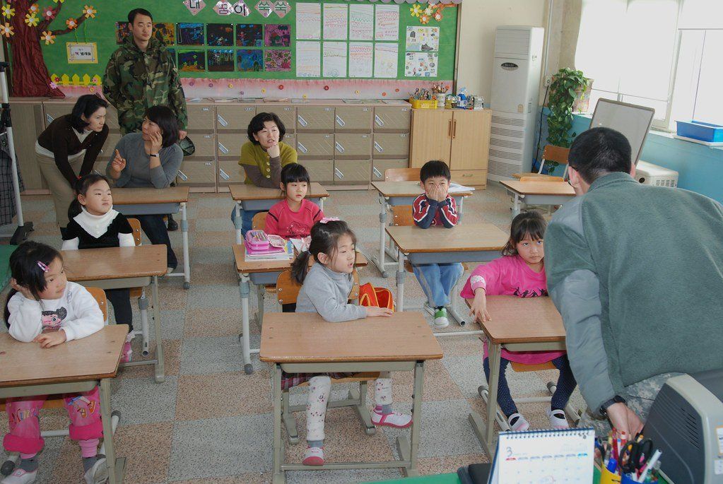 Lớp học tiếng Hàn với học viên ngồi theo bàn, giáo viên đứng hướng dẫn