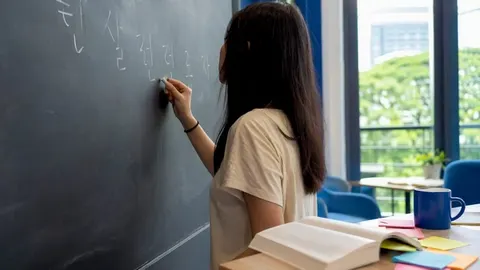 Giáo viên viết mẫu câu tiếng Hàn lên bảng trắng trong một lớp học người lớn