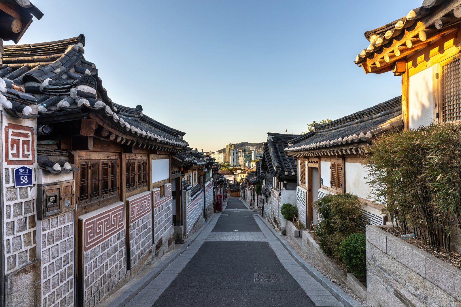 Con ngõ dốc Bukchon-ro 11-gil lúc bình minh, mái ngói hanok đổ dốc về phía đường chân trời Seoul