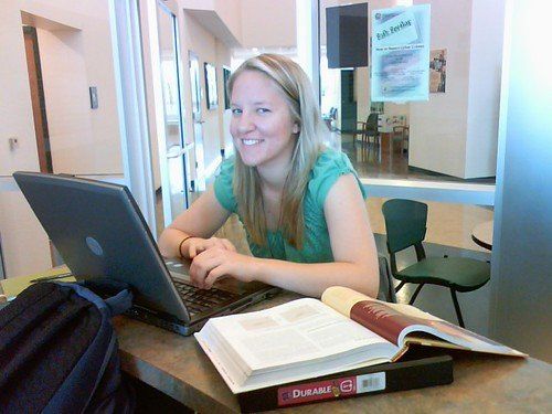 Một bạn nữ ngồi học với laptop và quyển giáo trình mở sẵn trên bàn