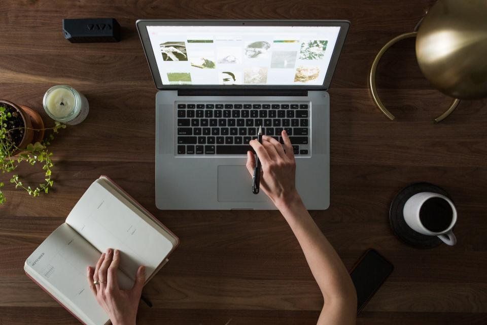 Bàn học nhìn từ trên xuống: laptop, sổ kế hoạch mở, ly cà phê và chậu cây nhỏ