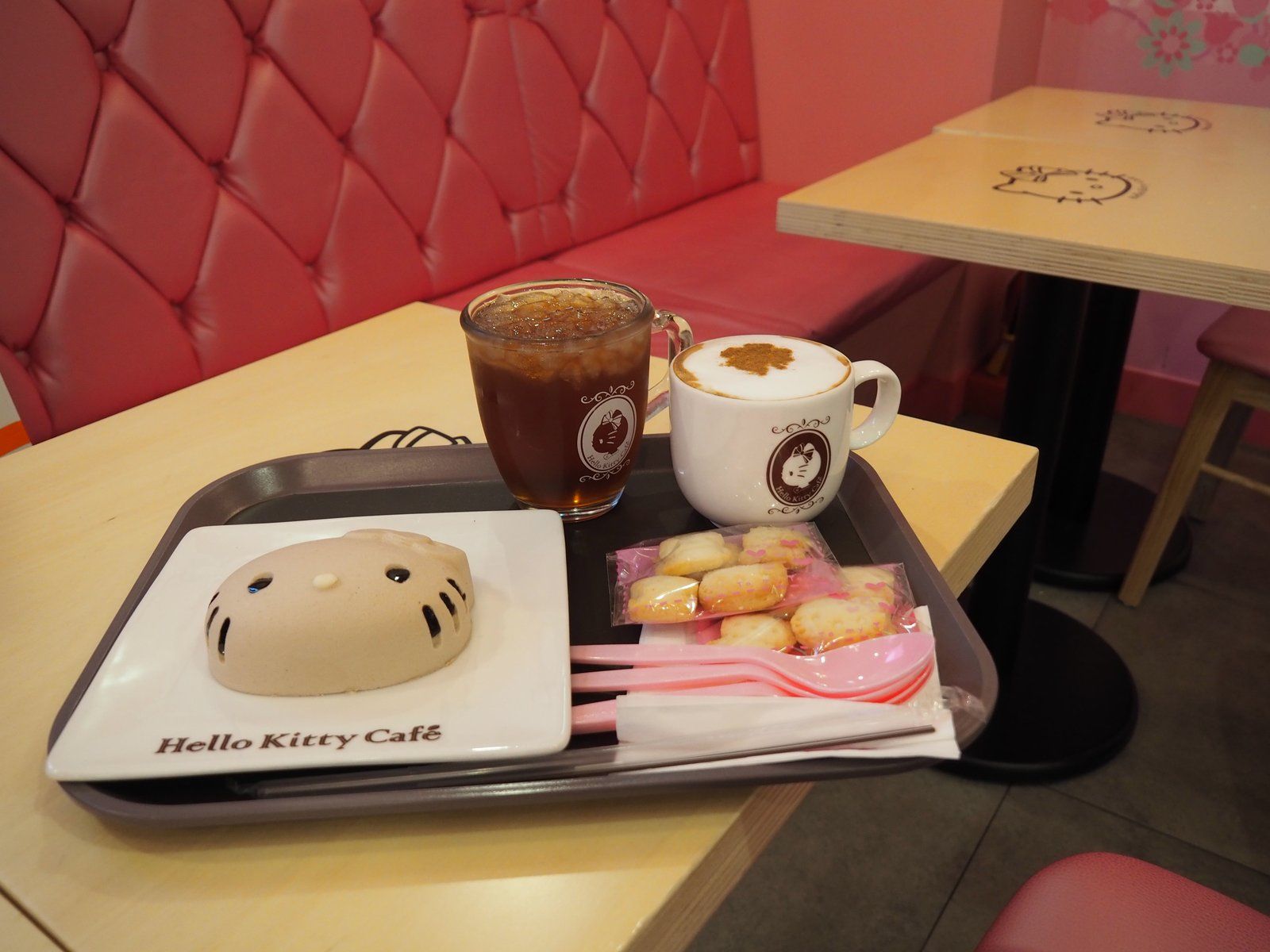 Khay đồ uống và bánh hình mèo Hello Kitty trên bàn ghế hồng trong một quán cà phê chủ đề
