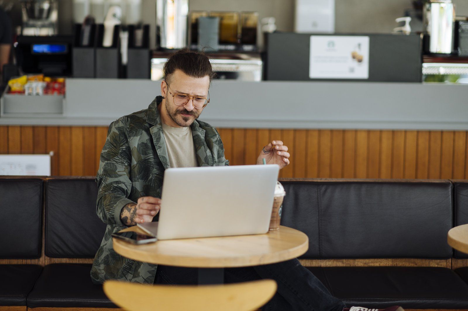 Một người đàn ông ngồi làm việc với laptop và ly cà phê đá trong quán