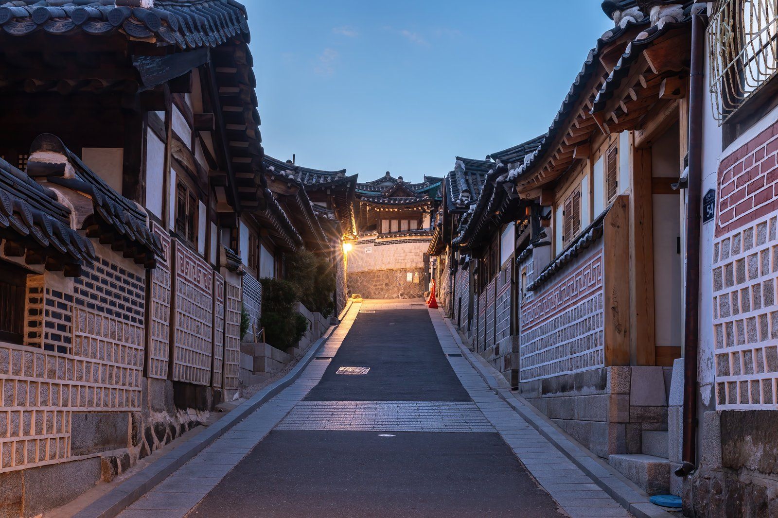 Con ngõ hanok ở làng Bukchon vào giờ xanh, cuối ngõ là một cổng cổ rực sáng