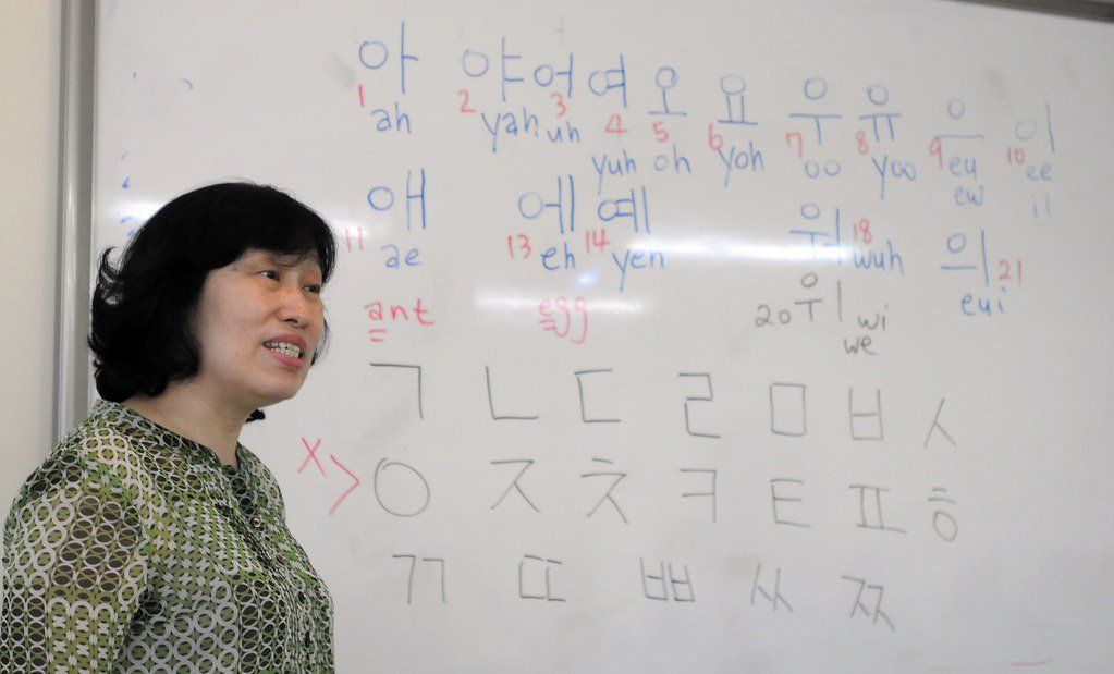 Một giáo viên đứng cạnh bảng trắng kín các nguyên âm và phụ âm bảng chữ cái Hangul trong giờ học tiếng Hàn nhập môn