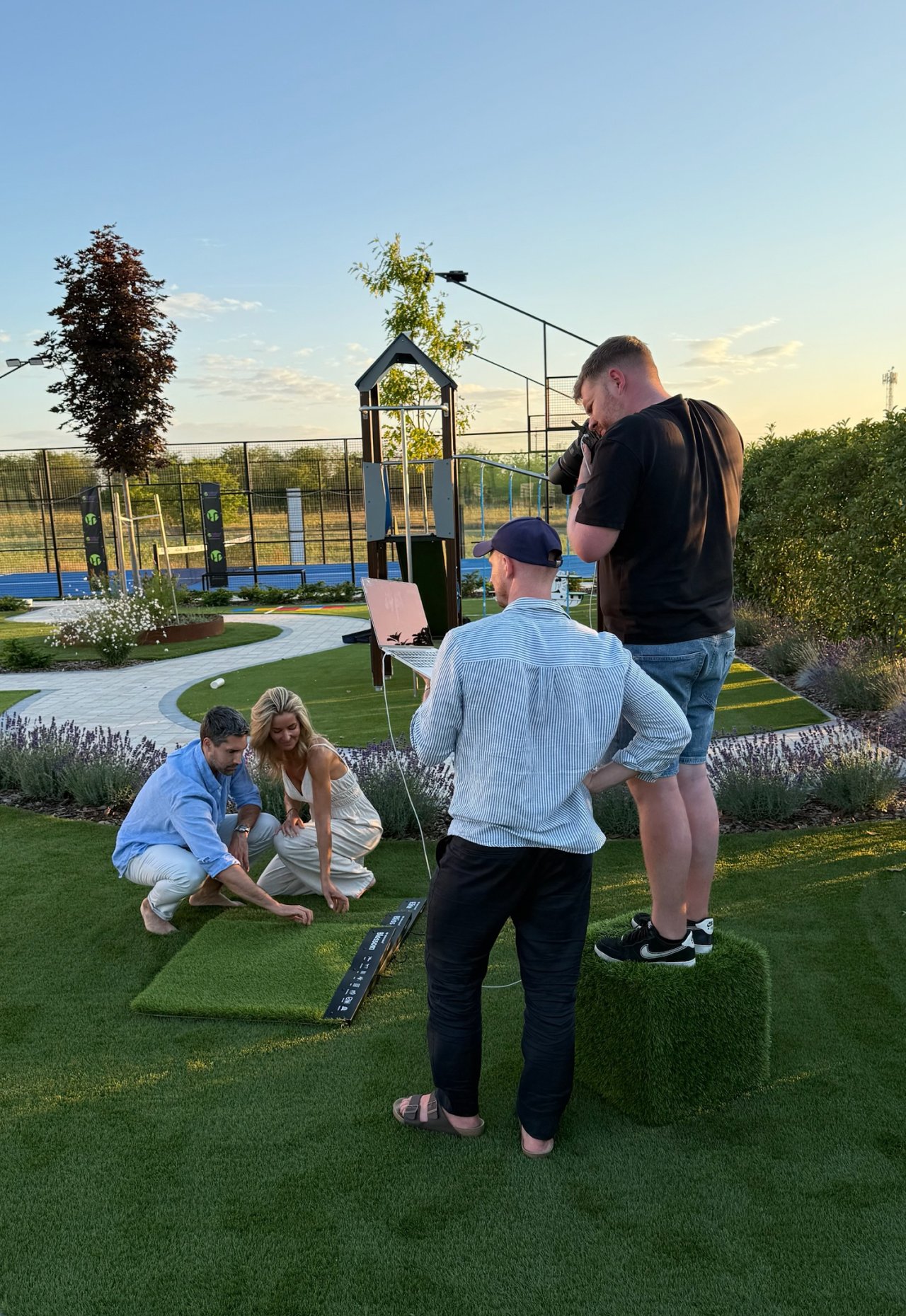 The team photographing a couple on a lawn at sunset, one holding a camera, another steadying a laptop