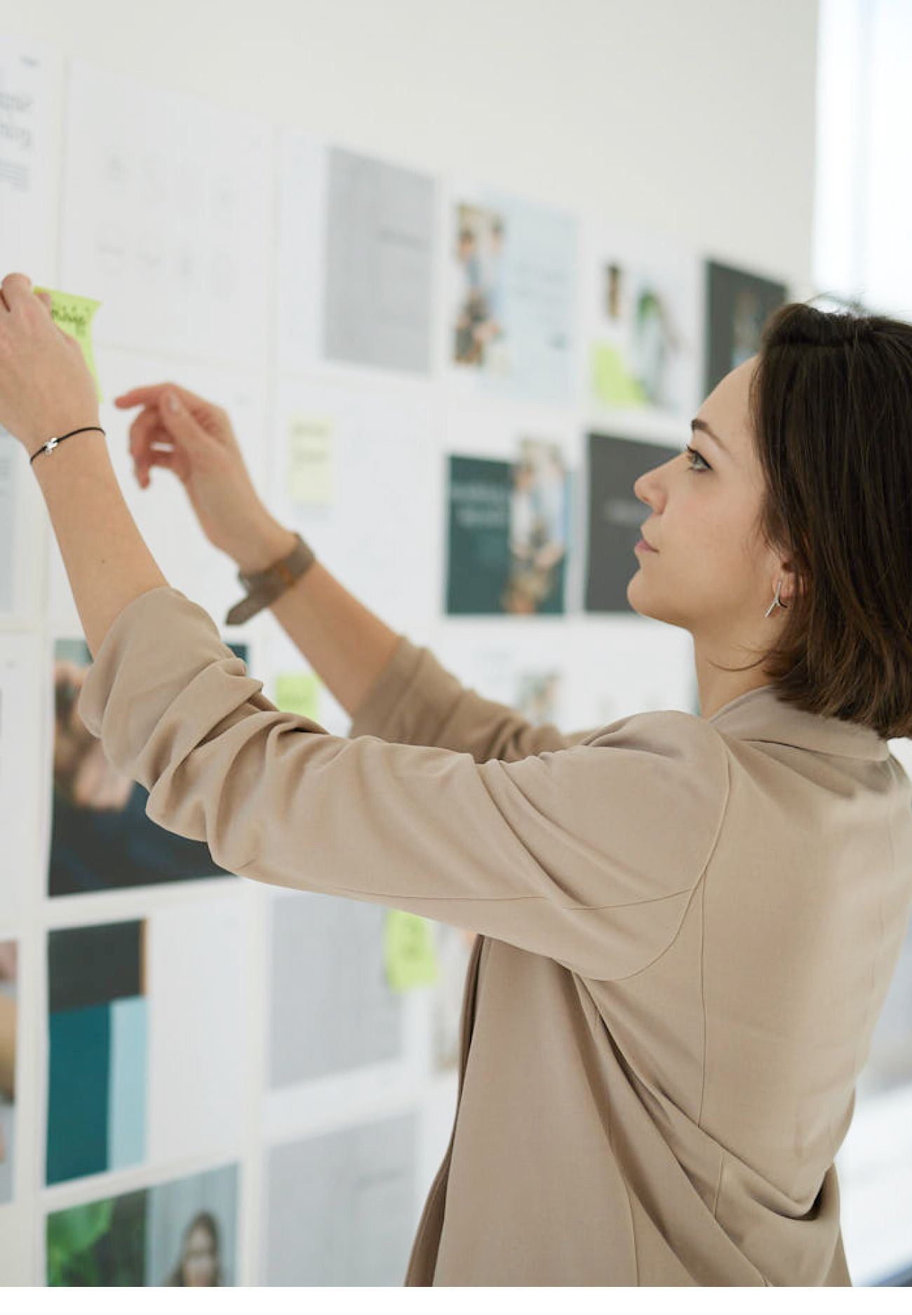 A designer reaching up to place a sticky note on a wall of printed layouts
