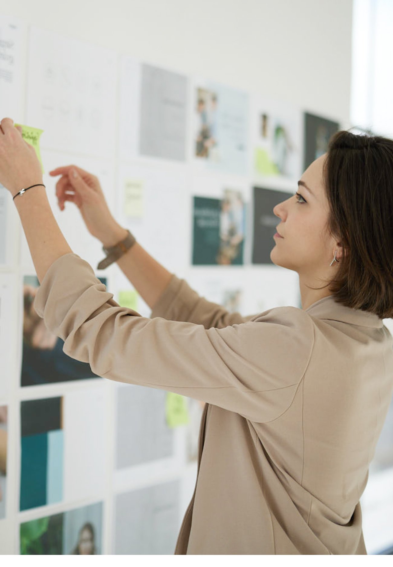 A designer reaching up to place a sticky note on a wall of printed layouts