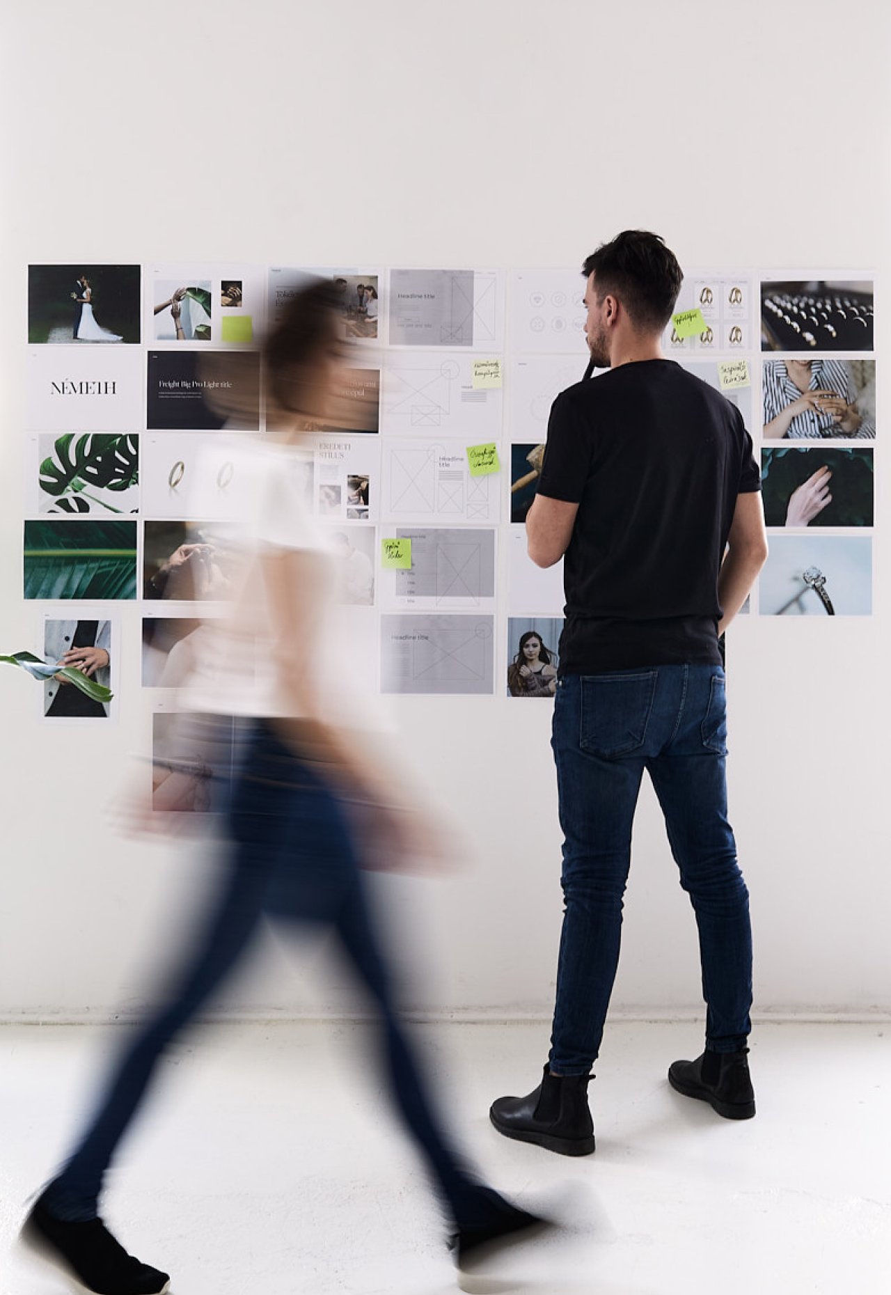 A designer studying a wall of printed layouts while a colleague walks past in motion blur