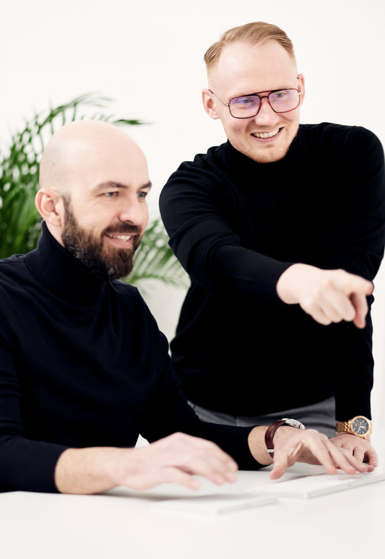 Two colleagues at a desk, one leaning in to point at something off screen, both laughing