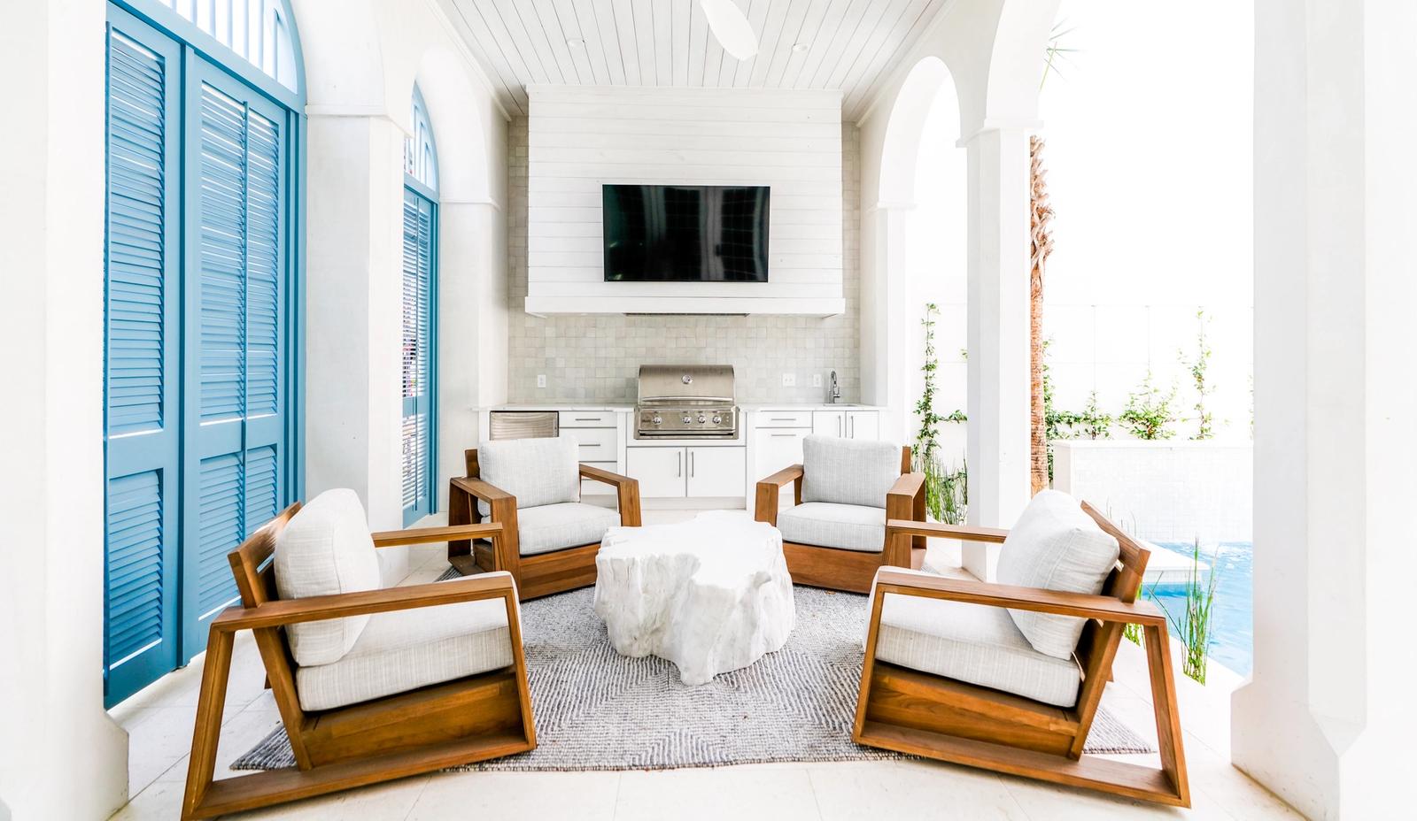 White coastal loggia with a built-in grill, wall-mounted TV and teak lounge chairs