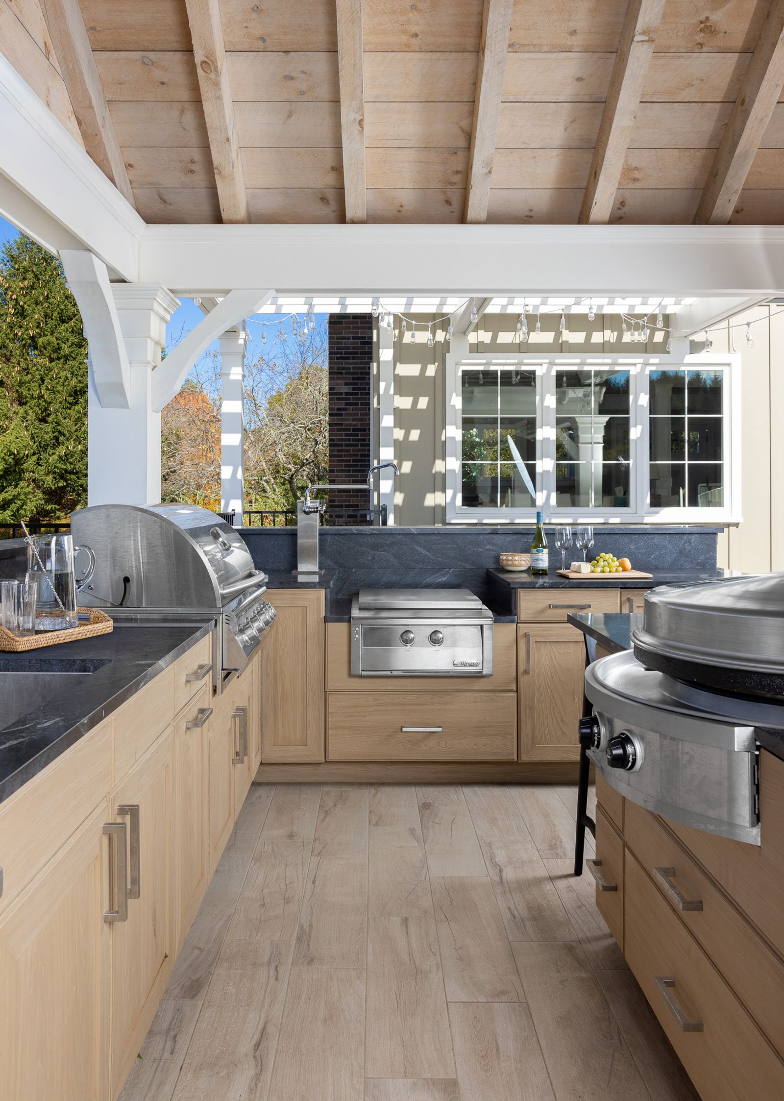 outdoor kitchen under a timber pavilion with two built-in grills and stone counters