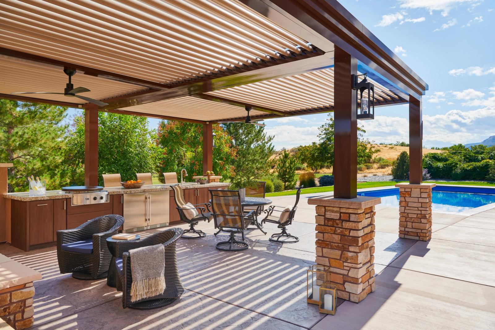 Poolside outdoor kitchen and dining area under a louvered pergola