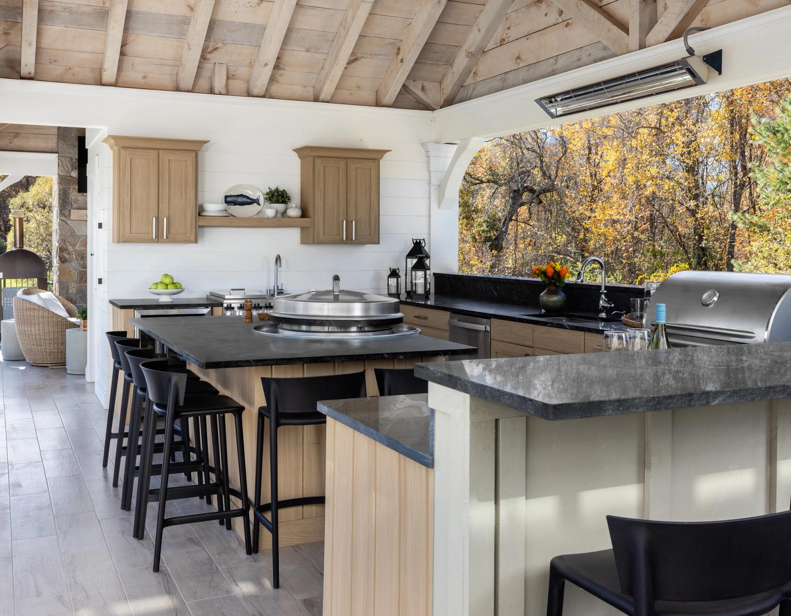 Covered pavilion kitchen in pale oak cabinetry with dark stone counters