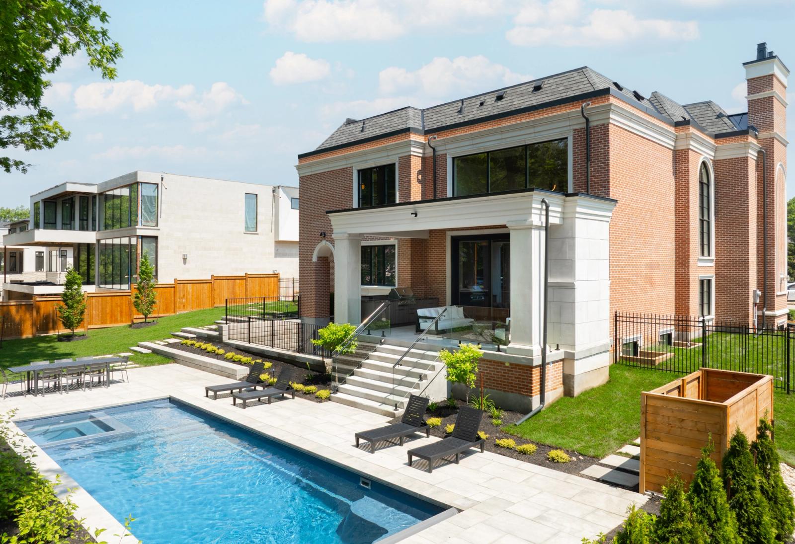 Brick home with a covered terrace, rectangular pool, sun loungers and cedar planters in the garden