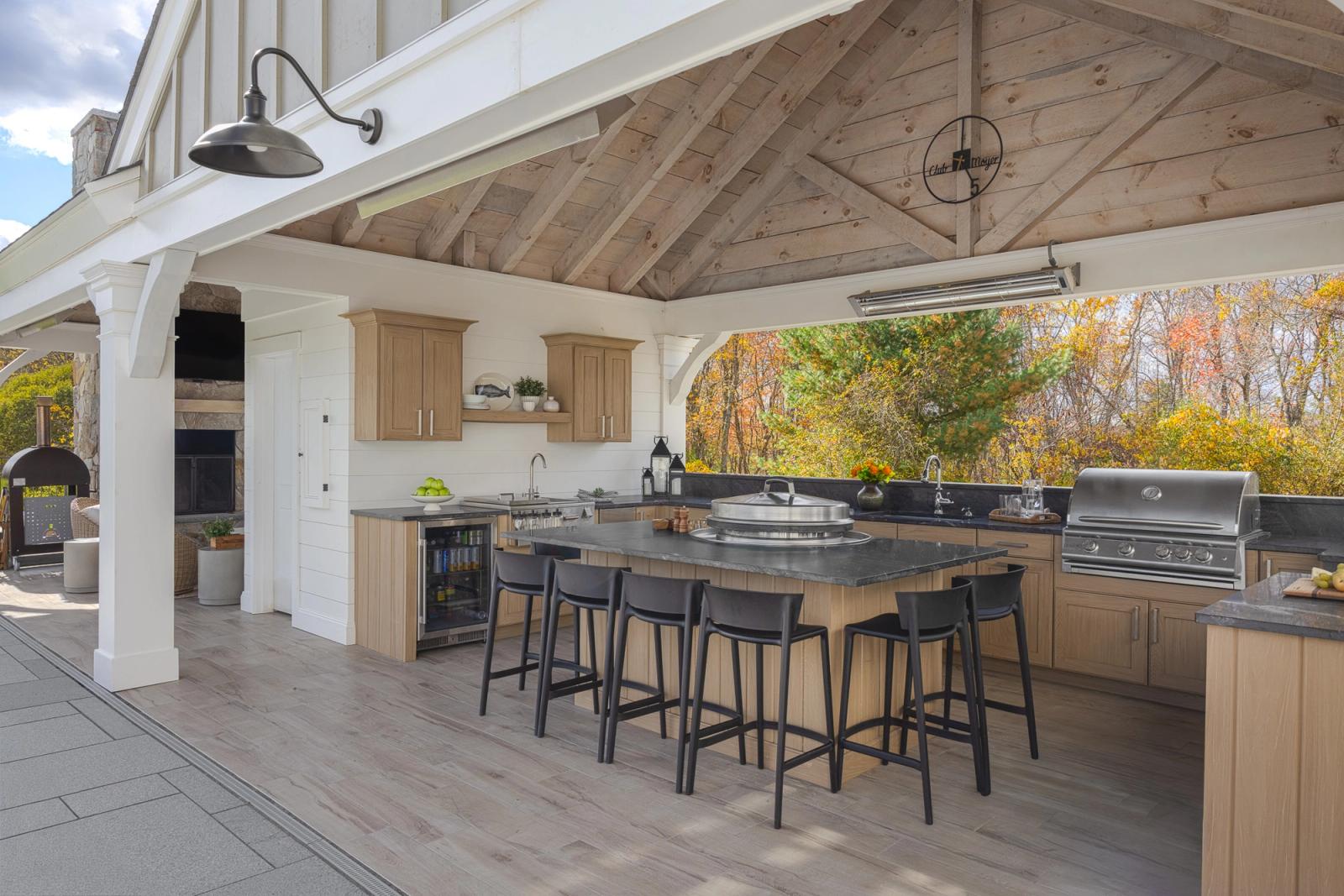 Outdoor kitchen island with black stools under timber pavilion