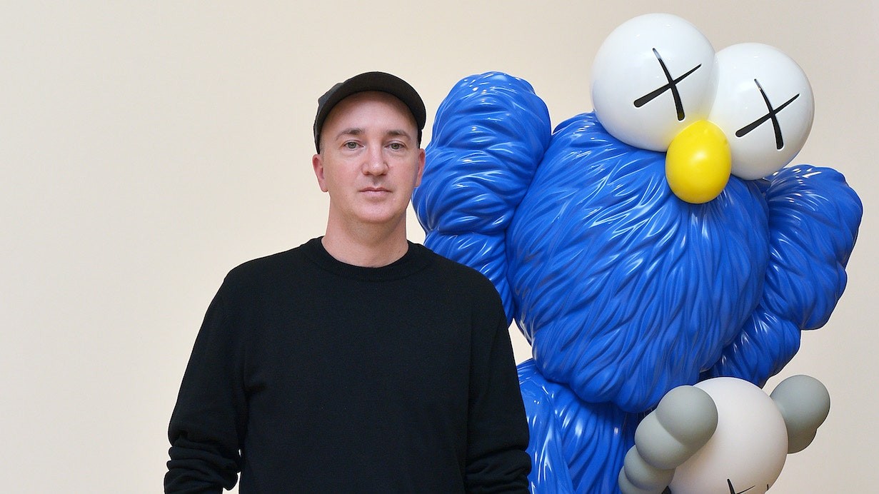 KAWS poses next to his large-scale sculpture