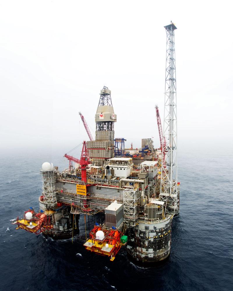 The Heidrun platform in fog on the Norwegian Sea, its flare tower rising far above the deck and orange lifeboat stations hanging near the waterline.