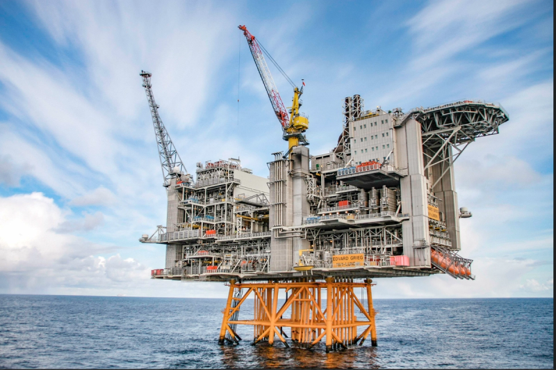 The Edvard Grieg platform standing on an orange steel jacket in calm open sea, cranes and a helideck extending out from the topside.
