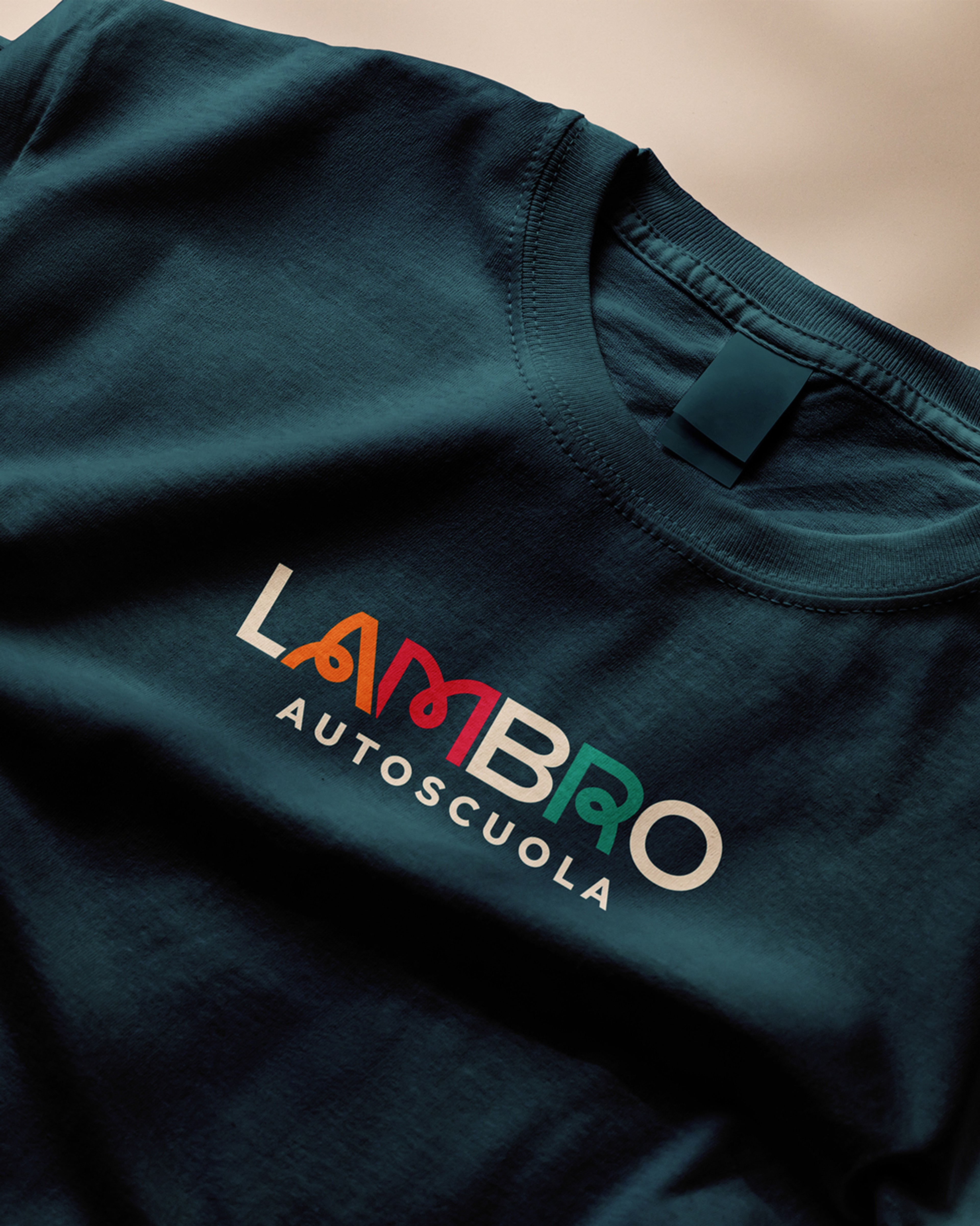 Dark teal T-shirt printed with the multicoloured Lambro Autoscuola logo
