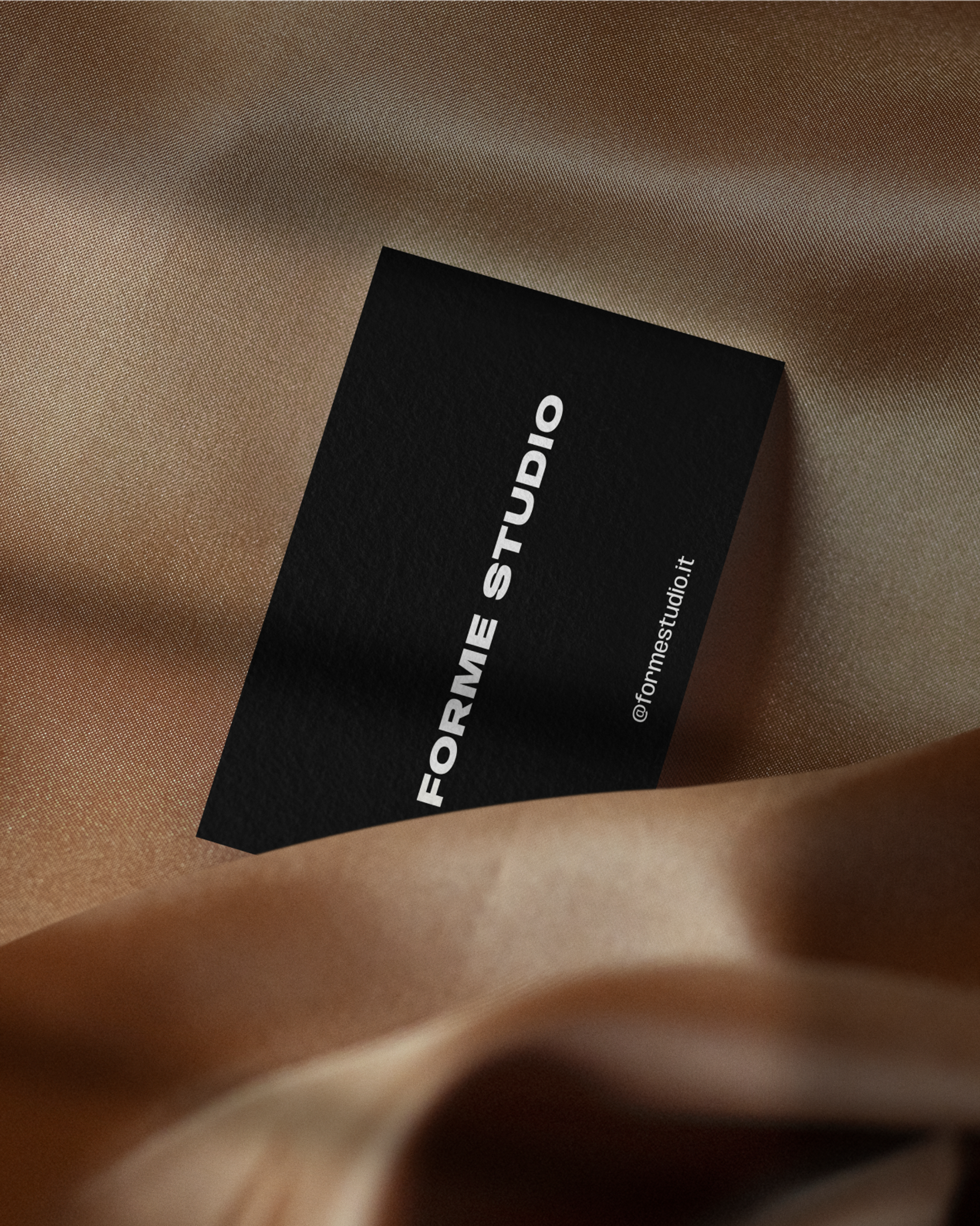 Black Forme Studio business card resting on bronze satin fabric