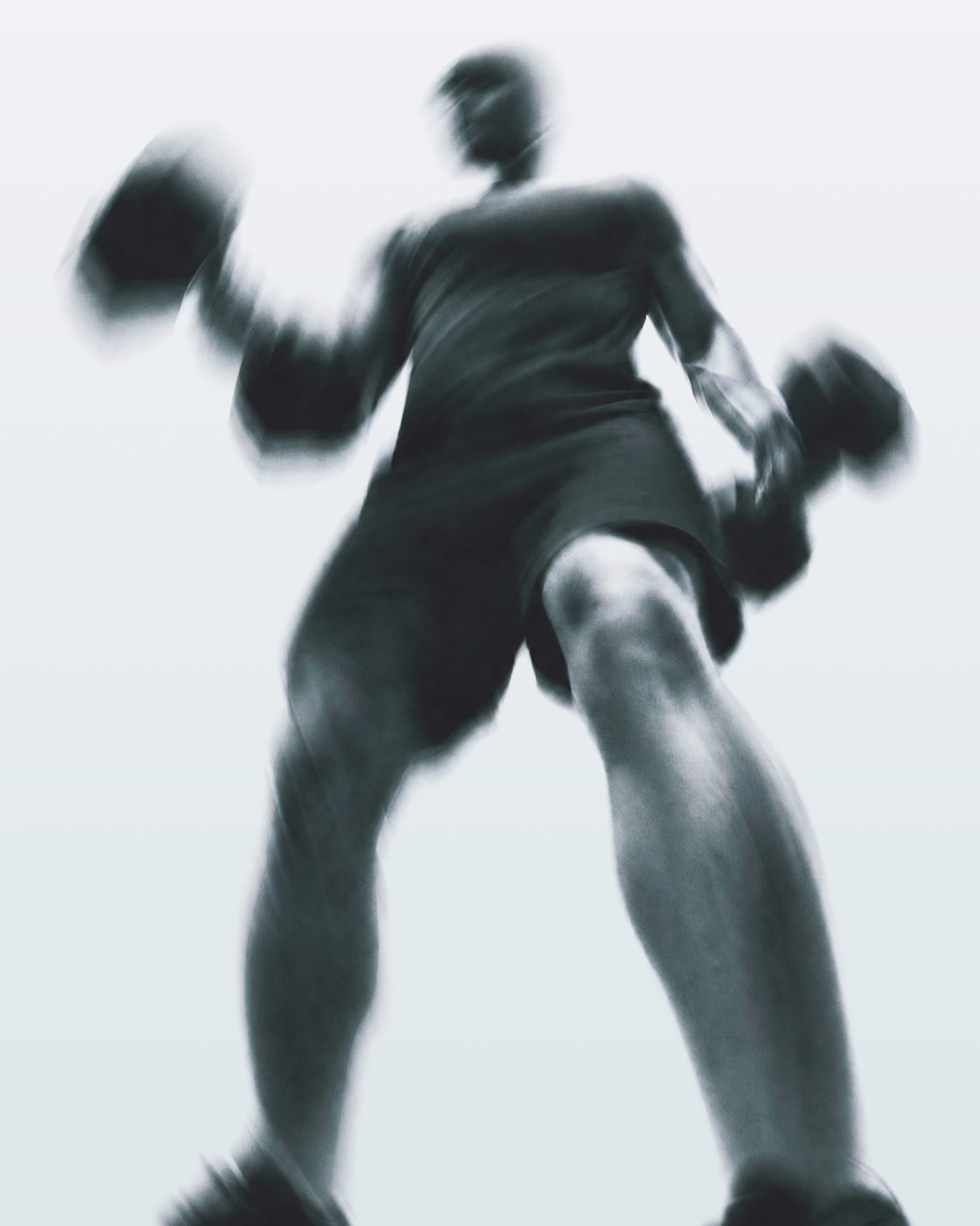 Wide-angle photograph from below of an athlete curling two dumbbells, motion-blurred, black and white.