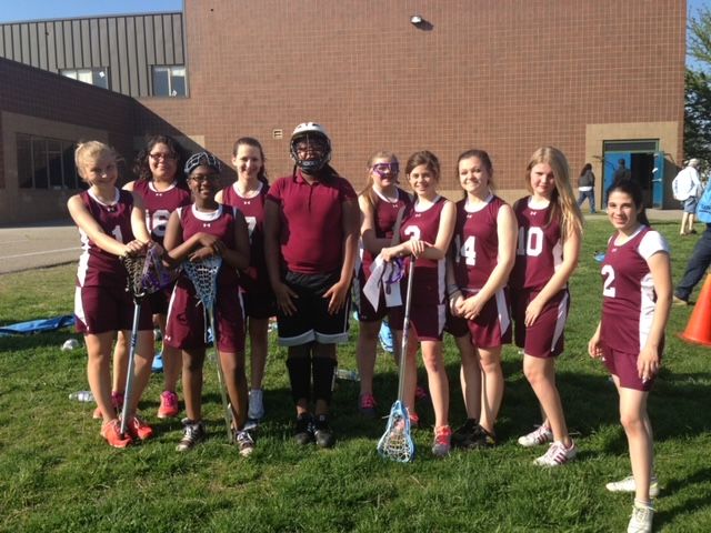 A girls lacrosse team, in their uniforms smiling for the camera.