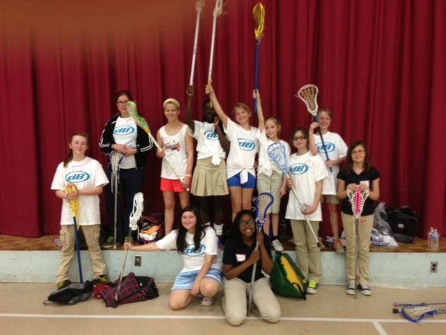 A group of girls in lacrosse uniforms holding their sticks. 