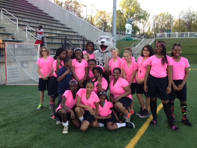A group of teens, wearing matching pink t-shirts posing with a costume mascot.