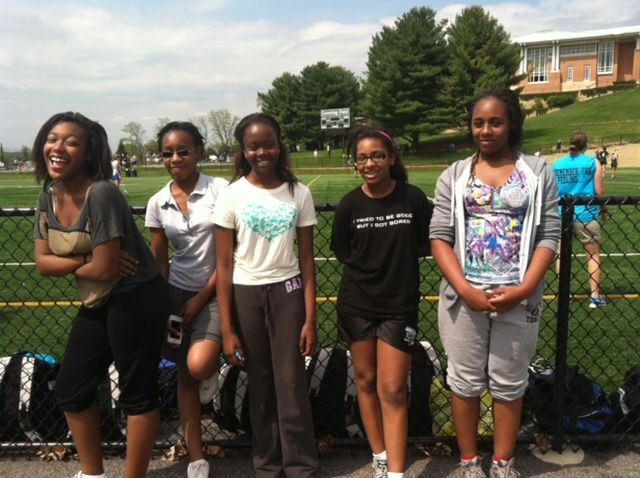 A group of teen girls smiling for the camera standing in front of a fence.