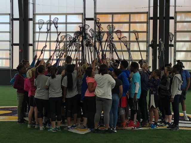 A group of young girls holding their lacrosse sticks in the air together.