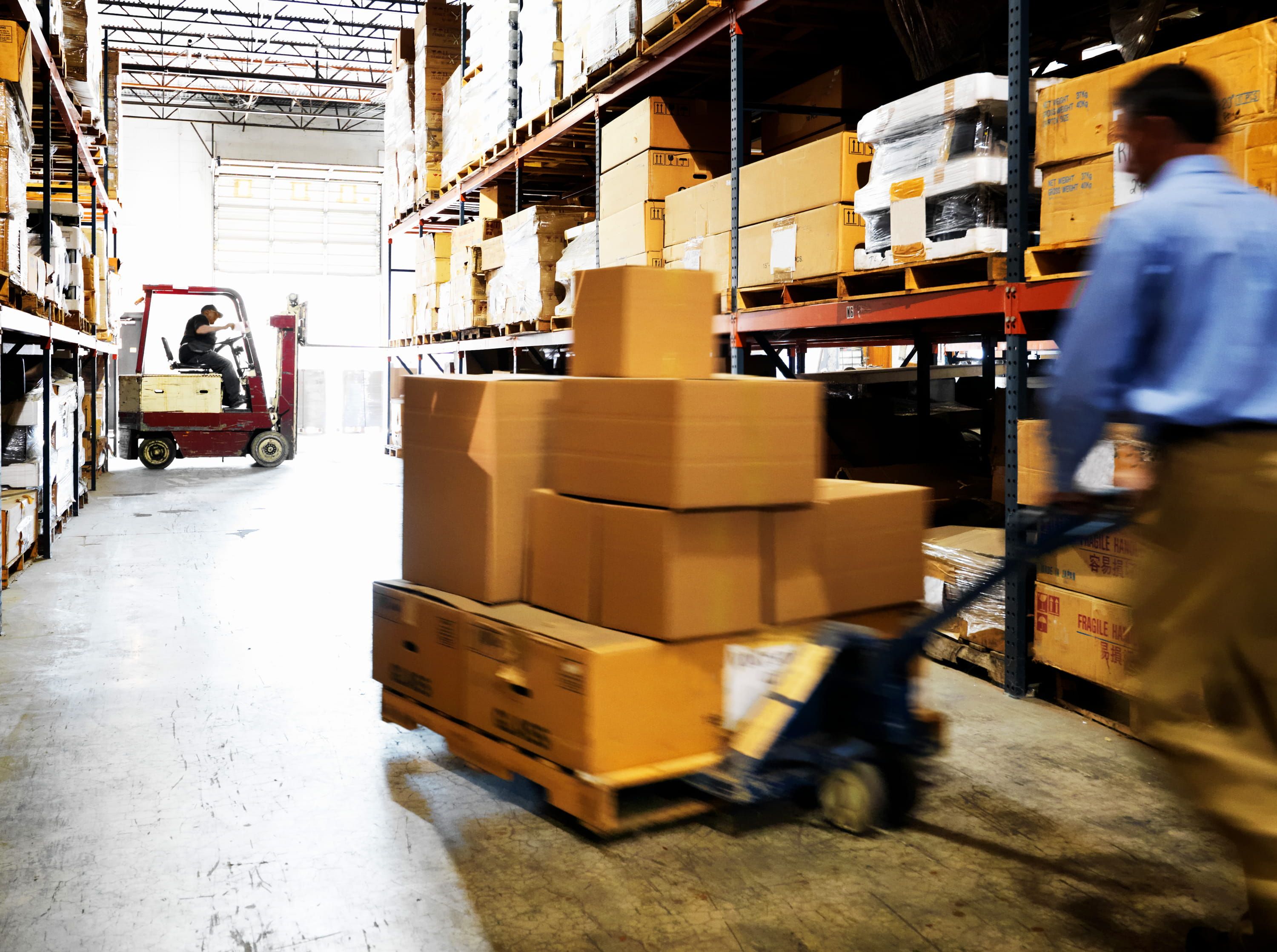 Man in khakis and blue shirt pushing pallet of boxes