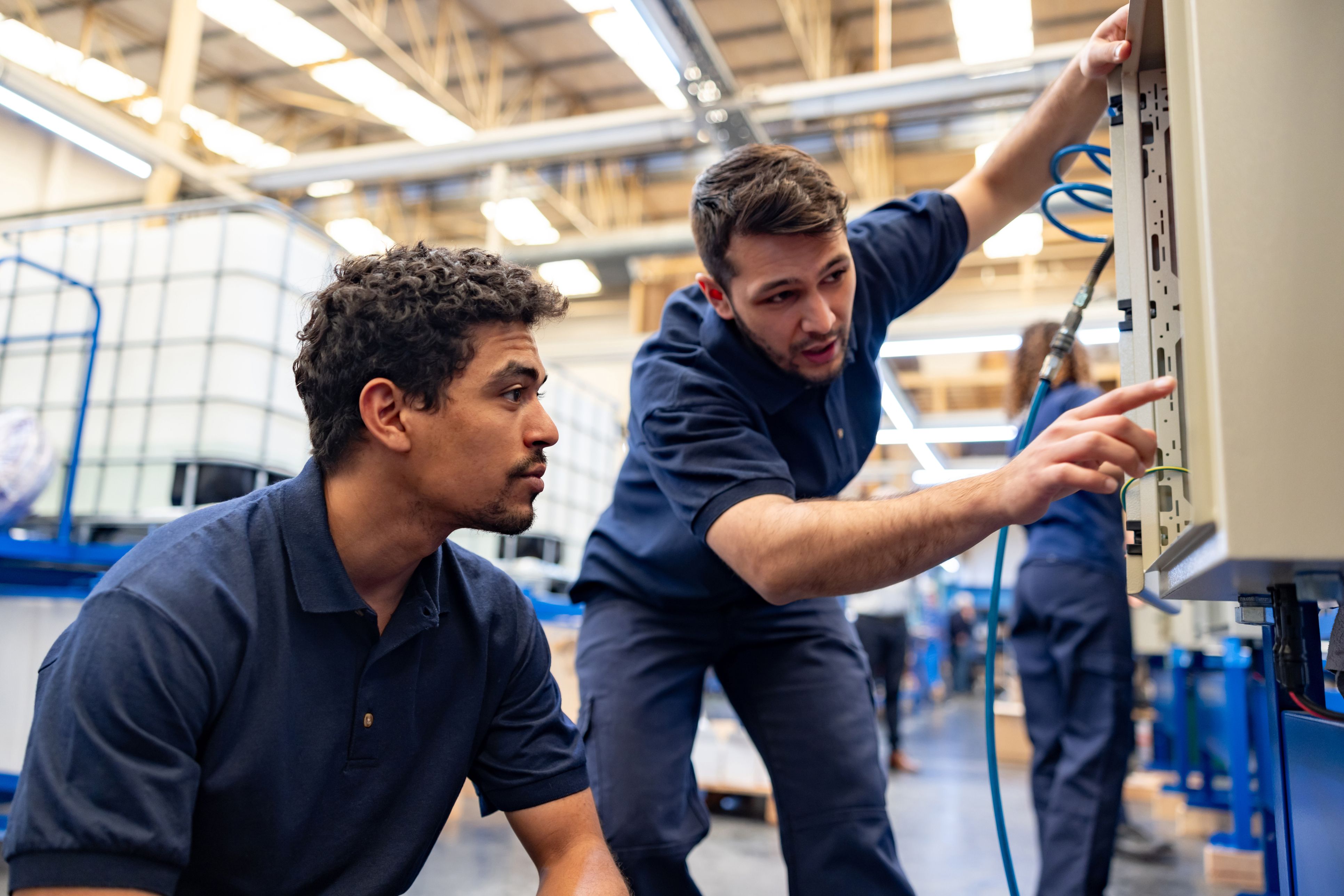 One male machinist showing another how to program machine