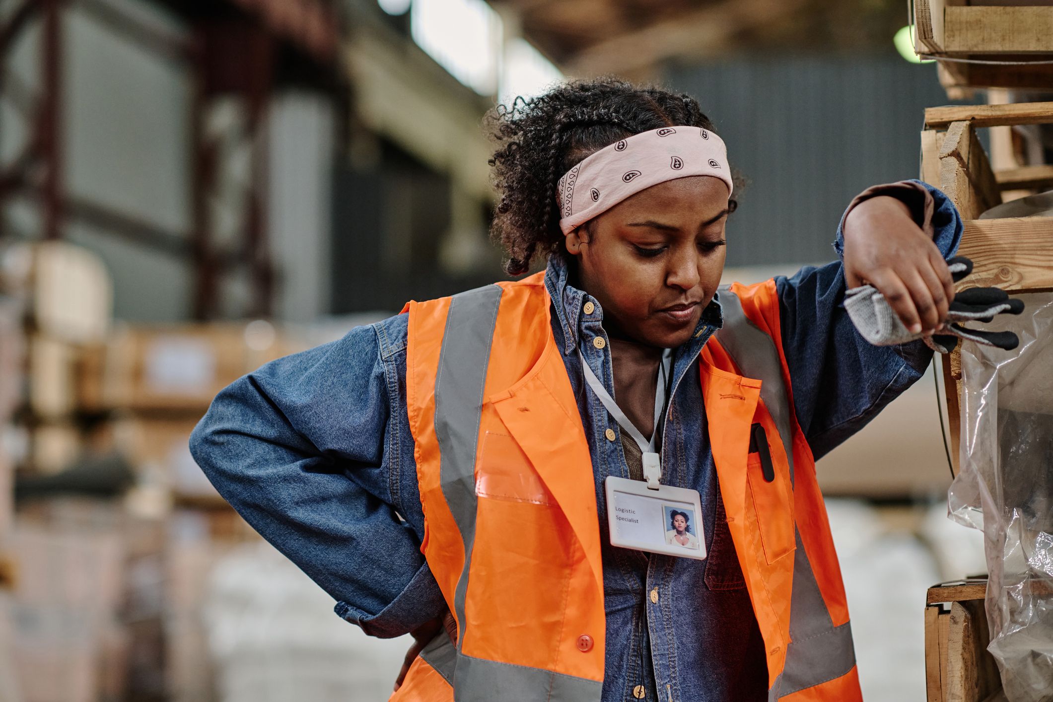 Black woman, hand on hip, leaning on a stack of pallets in a factory