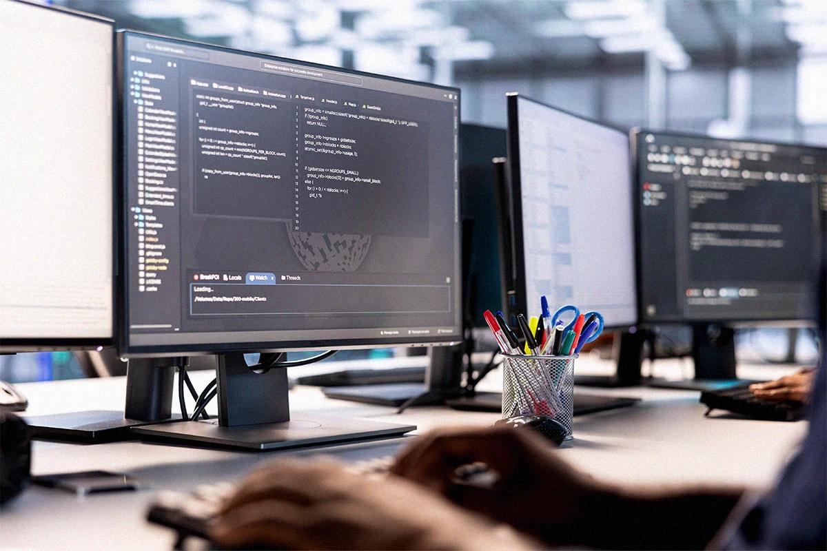 Hands writing code on multiple screens for web development