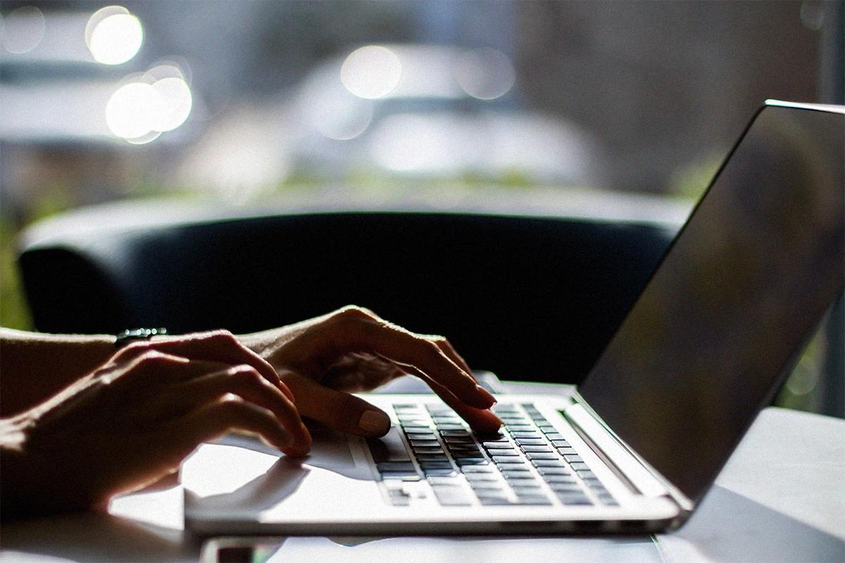Hands typing on a laptop with natural lighting in the background