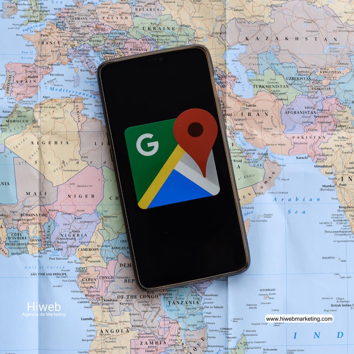 Vista de un teléfono móvil colocado sobre un mapa físico del mundo mostrando en pantalla el icono de Google Maps, representando geolocalización, navegación digital y uso de mapas y datos de ubicación en entornos tecnológicos y de marketing. Hiweb Agencia de Marketing.