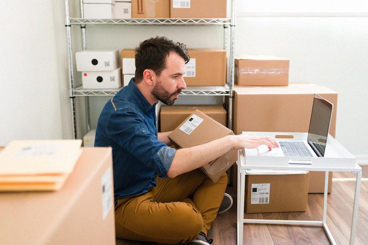 Person managing products and orders from a computer in a storage space, representing e-commerce operations and digital logistics Hiweb.