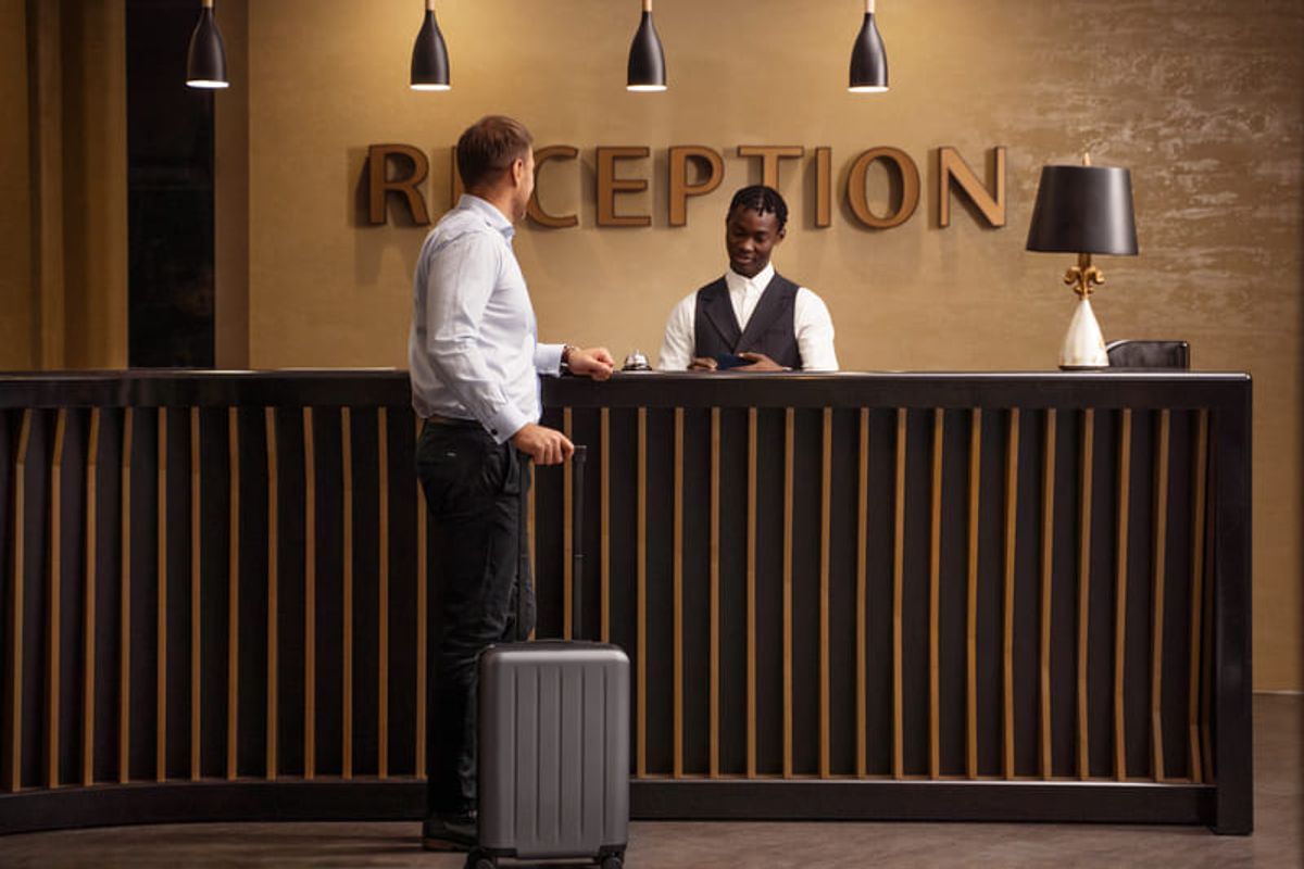 Hotel guest checking in at a reception desk with luggage, representing hospitality and tourism experiences Hiweb