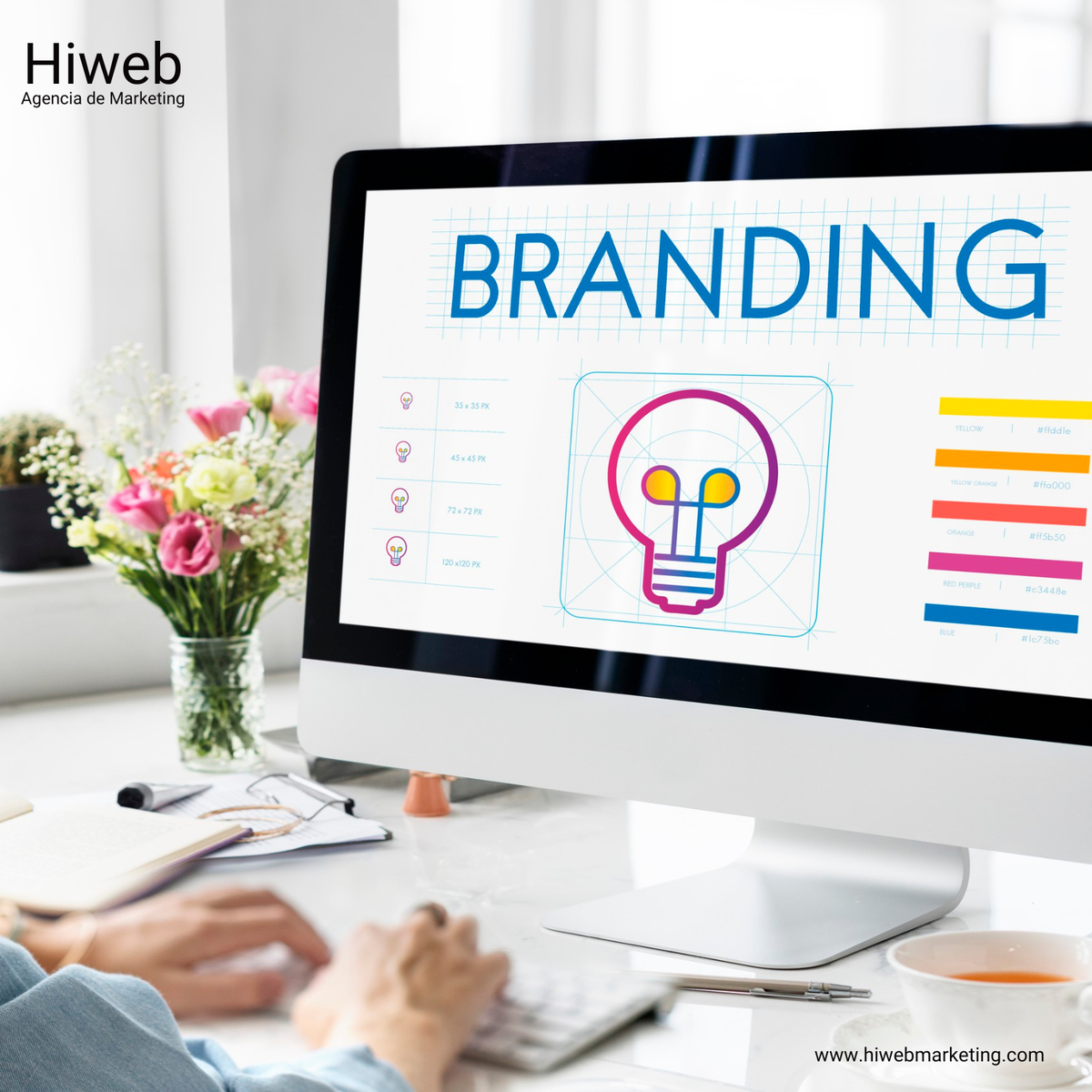 Marketing-focused workspace image showing a computer screen with the word “BRAND” in design grid layout, a hand using a stylus, and a bright, organized office setting emphasizing branding and creative work. Hiweb