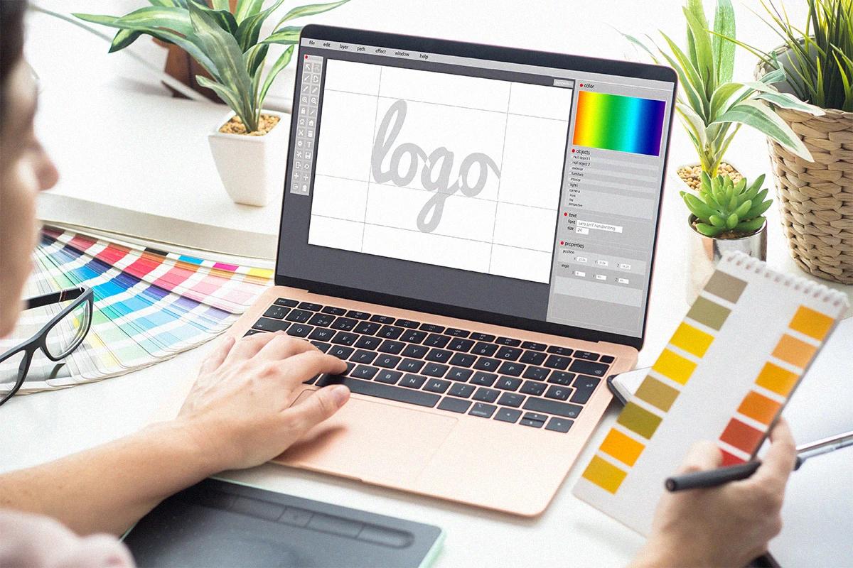 Persona diseñando un logo en un programa de diseño sobre un escritorio con una tableta gráfica y paletas de colores