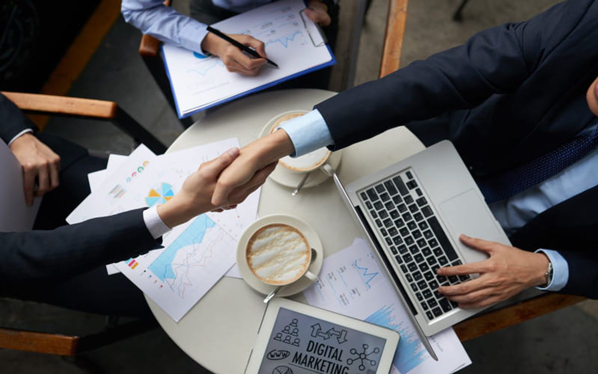 Profesionales de negocios estrechando manos durante una reunión representando alianzas, colaboración y acuerdos estratégicos Hiweb
