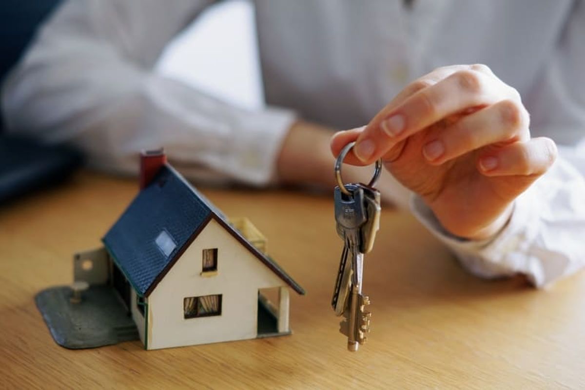 Primer plano de una persona sosteniendo llaves junto a una maqueta de casa representando compra y propiedad inmobiliaria Hiweb