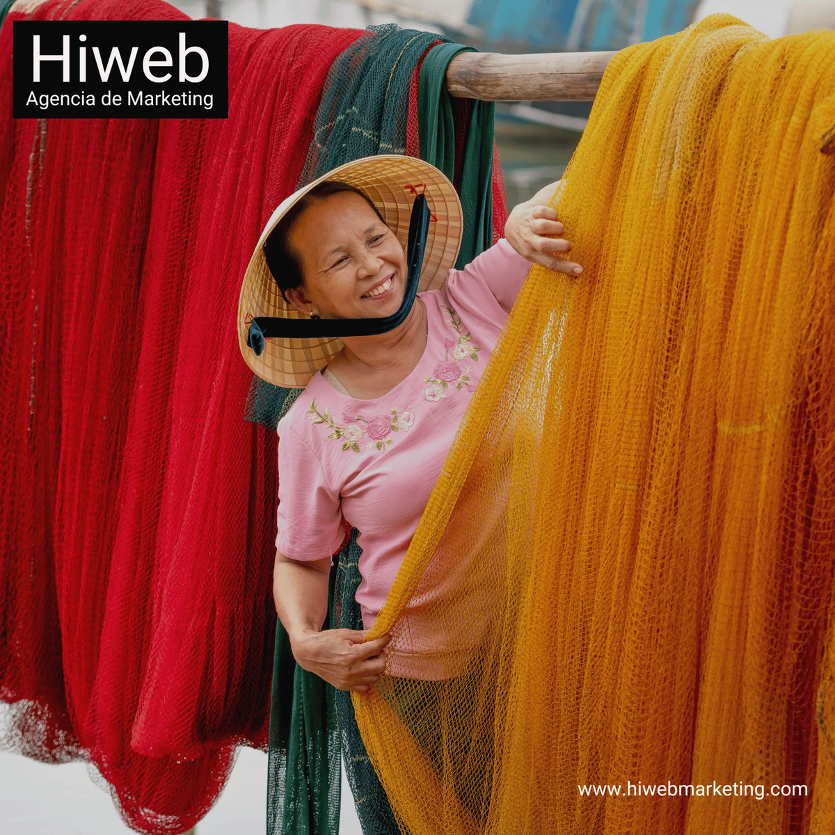 Mujer sonriendo mientras sostiene redes de pesca de colores rojo, verde y amarillo, representando trabajo artesanal tradicional. Hiweb Agencia de Marketing.